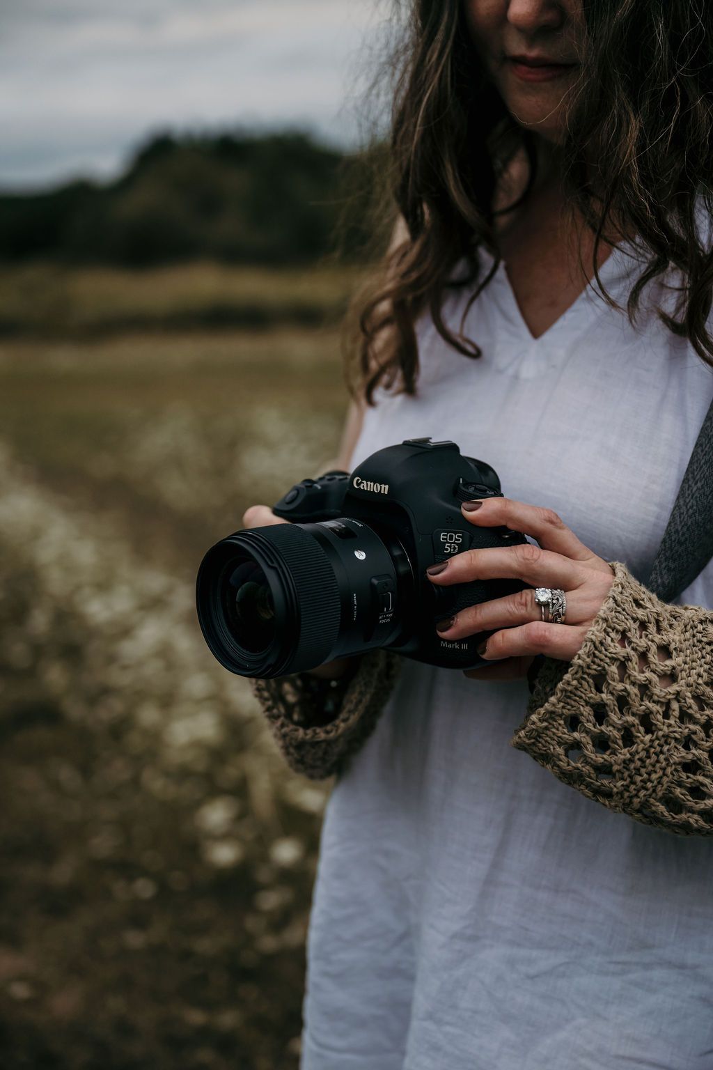 Close-up of your Bowmanvile, ON family photographer holding Canon camera while wearing knit sweater and white dress