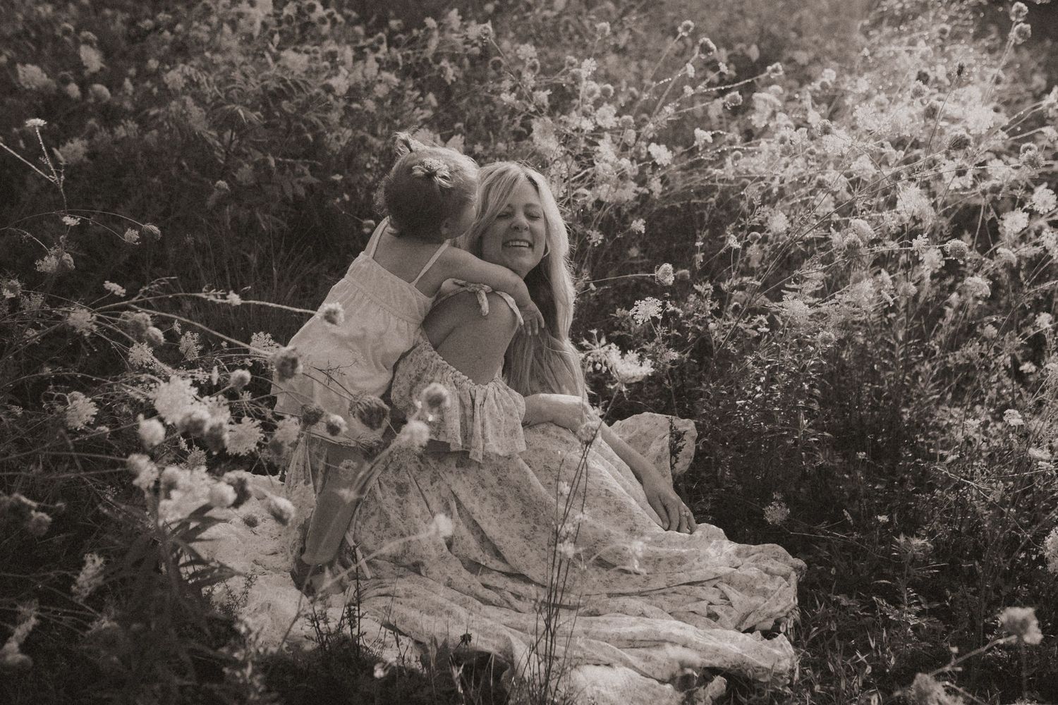 Black and white photo of a mom getting a hug from her daughter in a wildflower field by Durham Region motherhood photographer