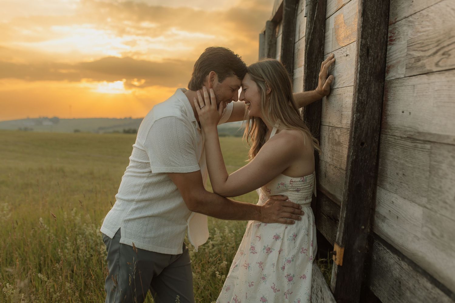 A couple leaning against a piece of old farm equipment in a field at sunset during an engagement shoot by wedding photographer Bowmanville