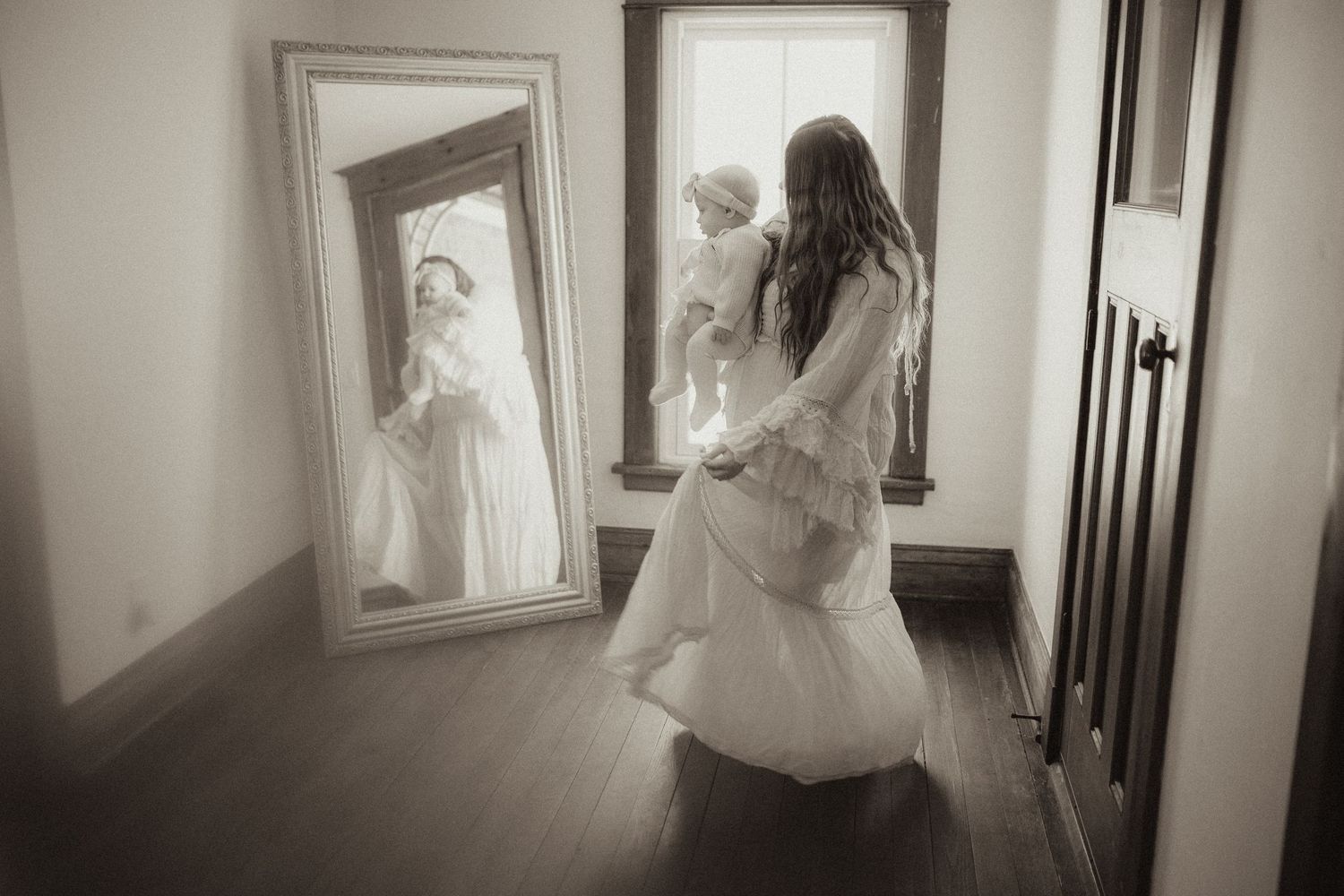 Black and white image of a mother dancing with her baby in her arms in front of a mirror in farmhouse by Orono, ON family photographer
