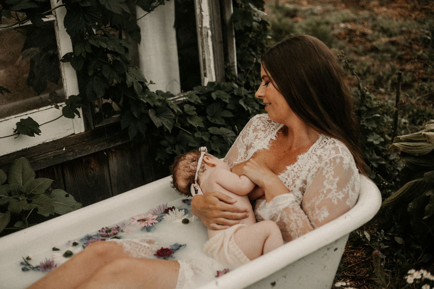 Mom nursing her baby in an antique tub having a milk bath outside in a lace kimono by Bowmanville, ON familyphotographer