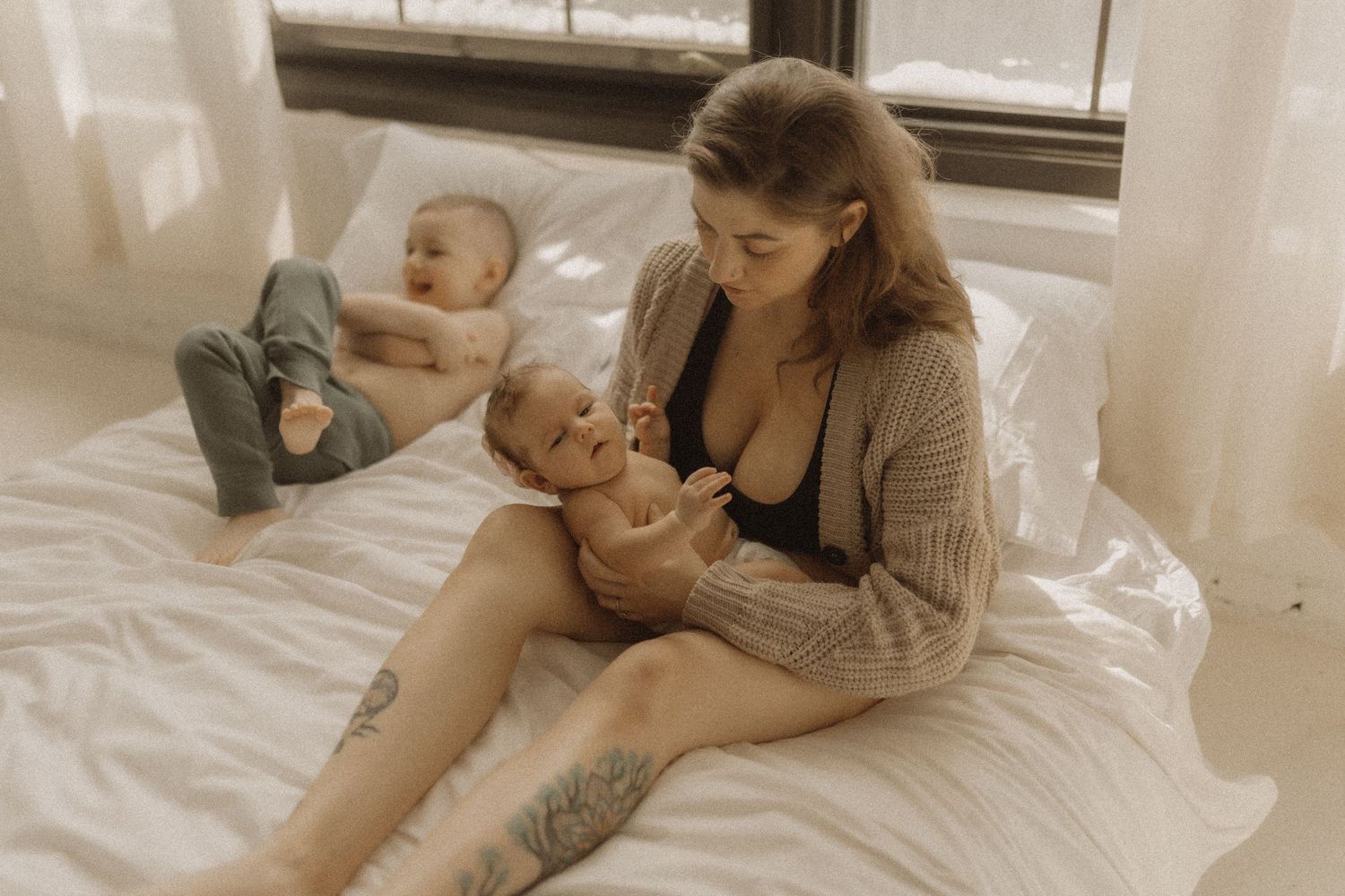 Mom gazing lovingly at her newborn while her older son lounges beside her on the bed by Bowmanville, ON family photographer