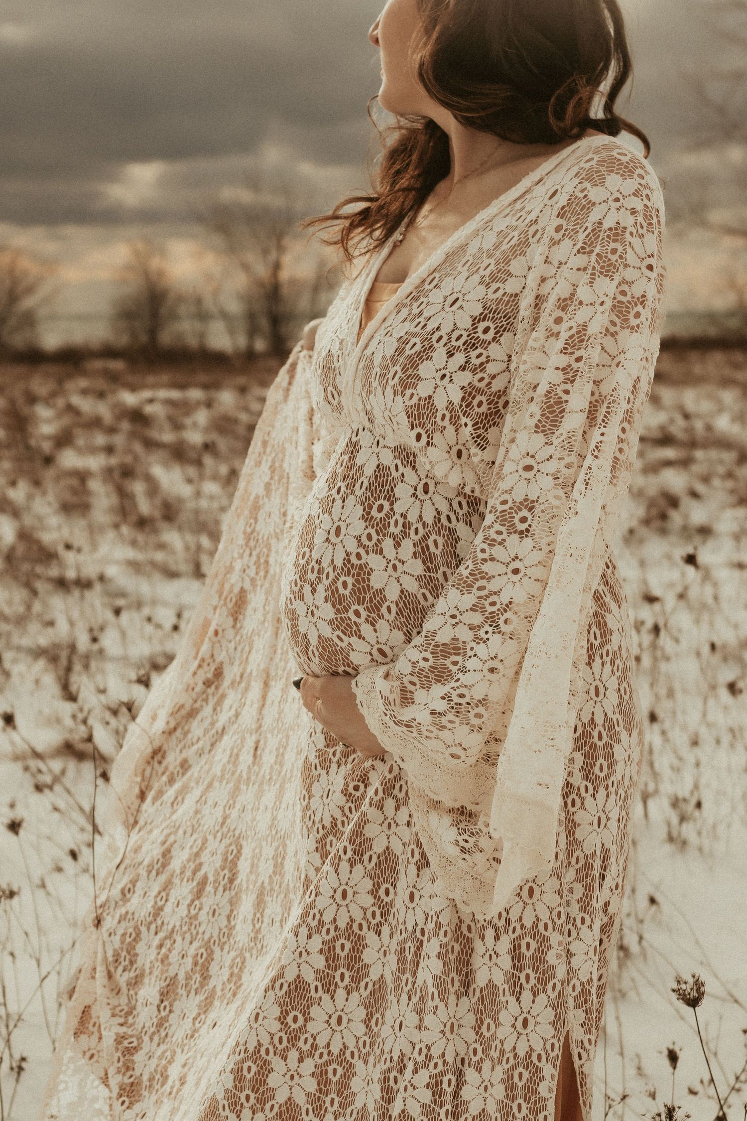 Dramatic photo of a mama-to-be cradling her baby bump on a winter beach in Bowmanville, ON