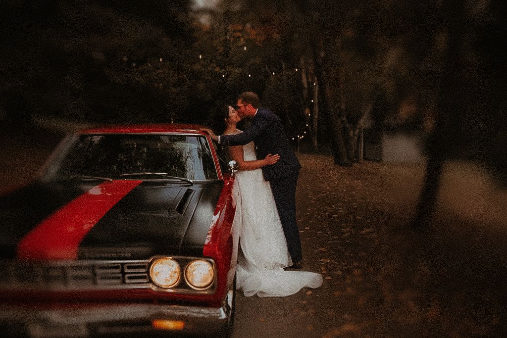 A couple after dusk sharing a kiss against an old car after a small wedding  by Cobourg Wedding and Elopement Photographer
