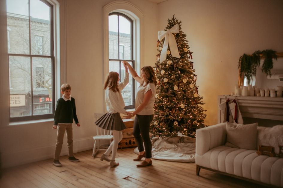 Family dancing together around a Christmas tree in a cozy holiday scene.