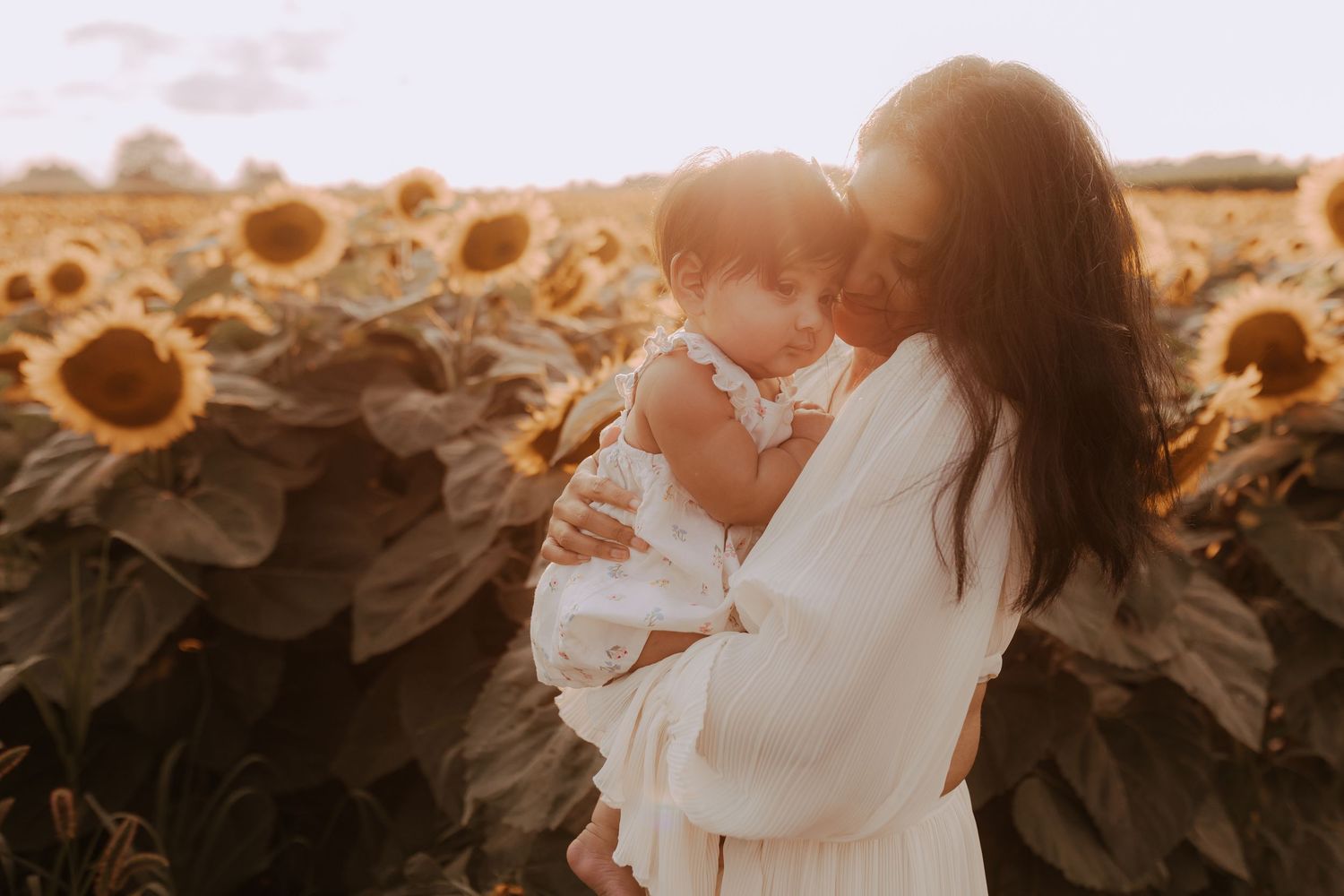 Mother cuddling her baby in a sunflower field during a motherhood photography session in Durham Region, Ontario
