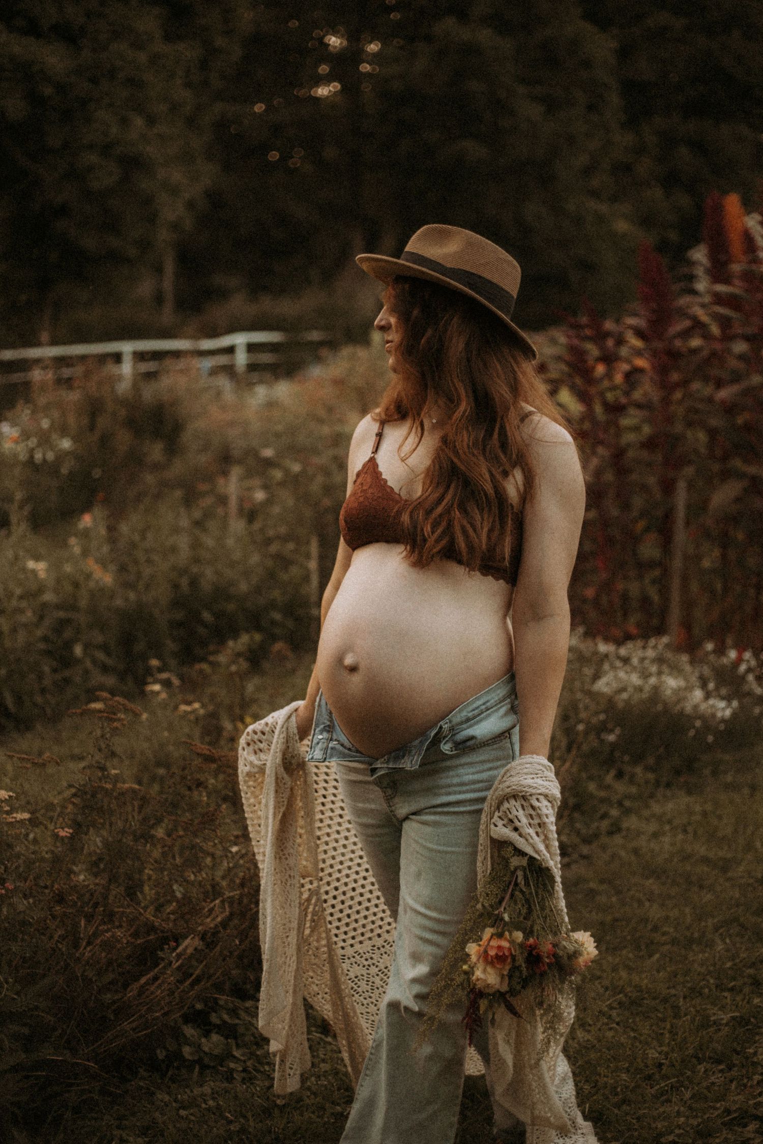 An expecting mom in a beige dress and cardigan holds a fall bouquet in a garden taken by Bowmanville, ON. family photographer