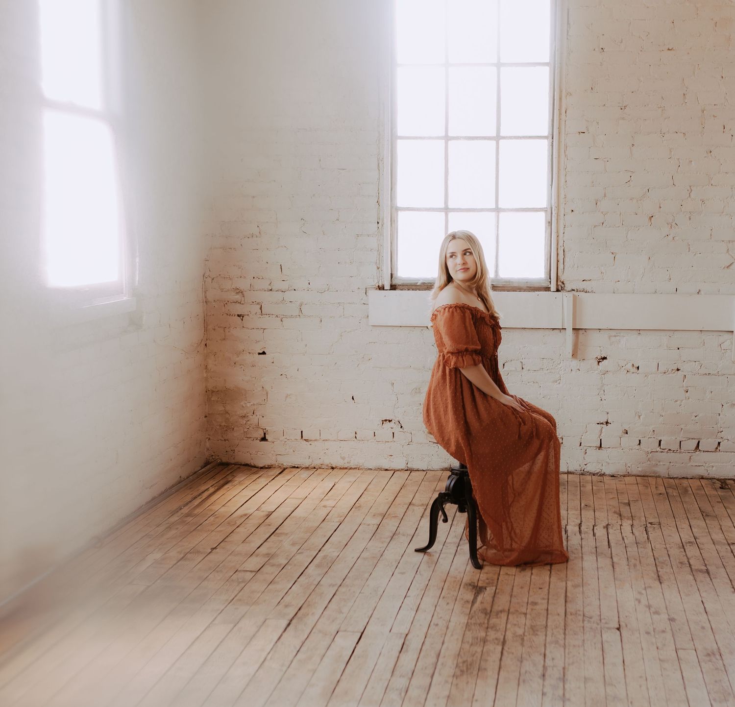 Figure in rust-colored dress creates dynamic poses in sunlit white studio space.
