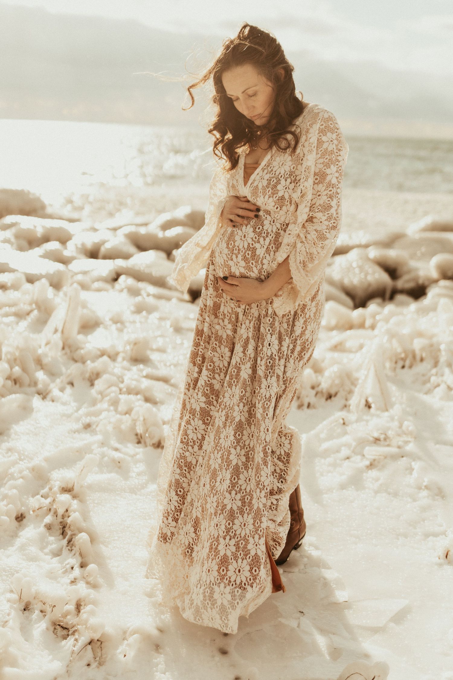 mom gazing down at her pregnant belly on a winter beach on a maternity photo shoot in Bowmanville, ON