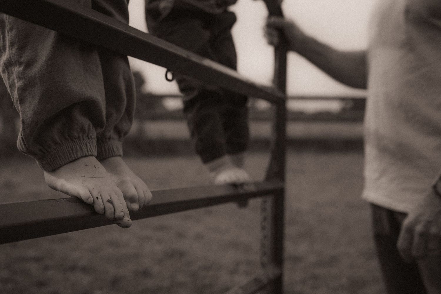 Detail shot of boys climbing a fence as their dad looks on by Durham region motherhood photographer