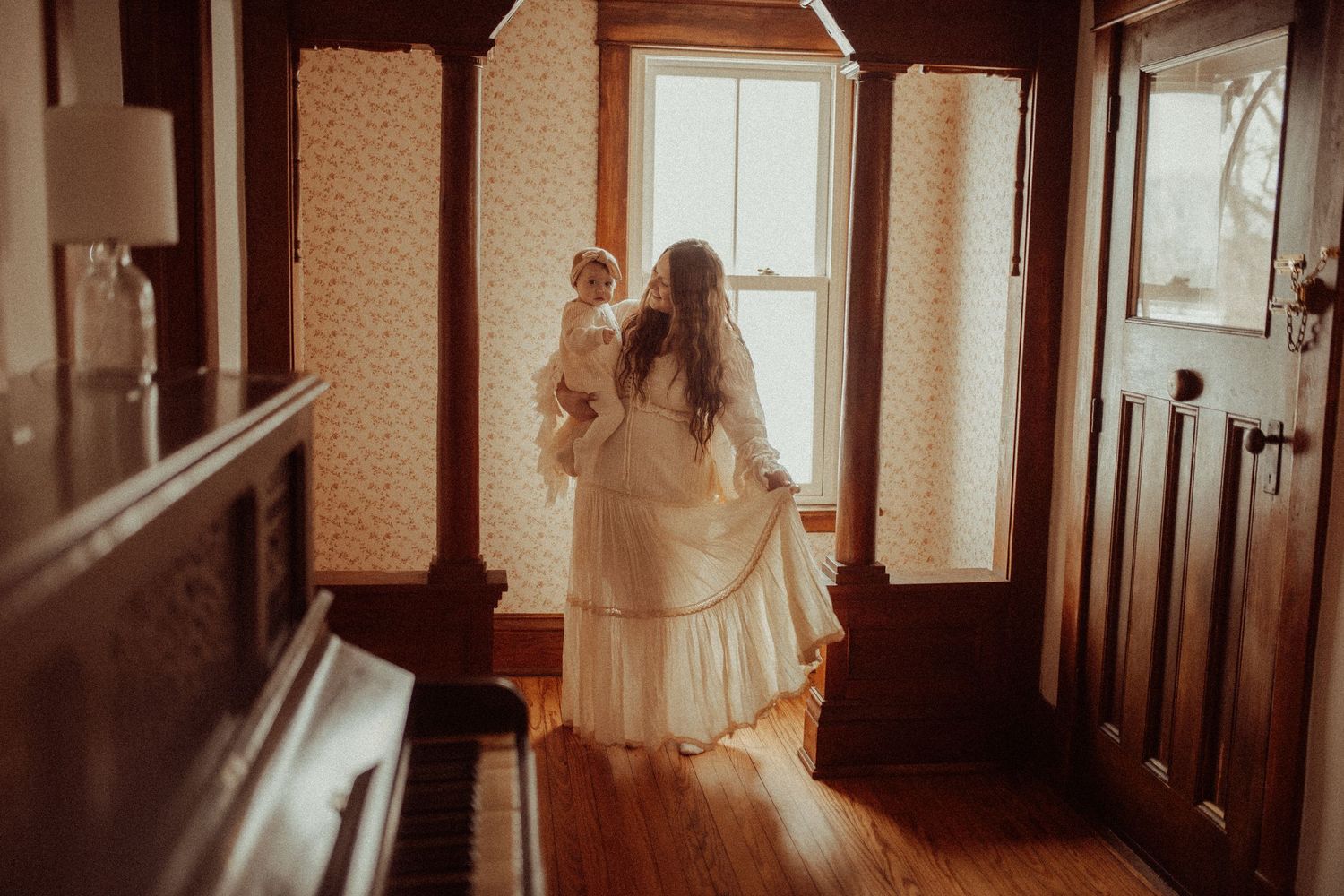 Mom in a flowing dress holding her baby in a farmhouse with golden light enjoying the moment by Orono, ON family photographer.