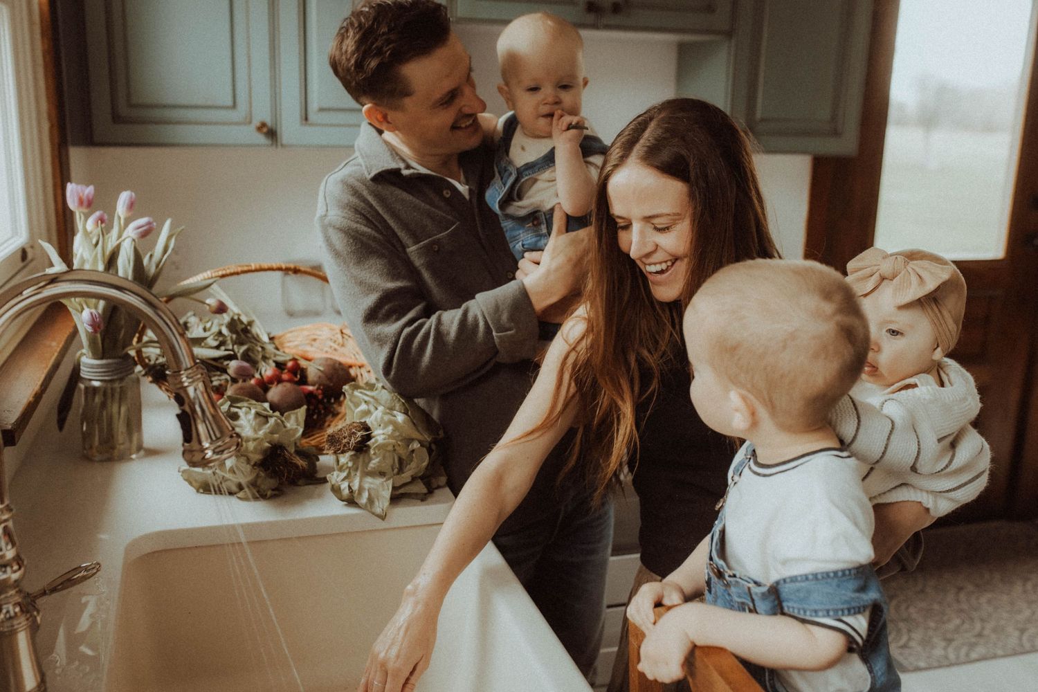 A young family working together at a farmhouse sink to wash vegetables by Durham Region maternity photographer