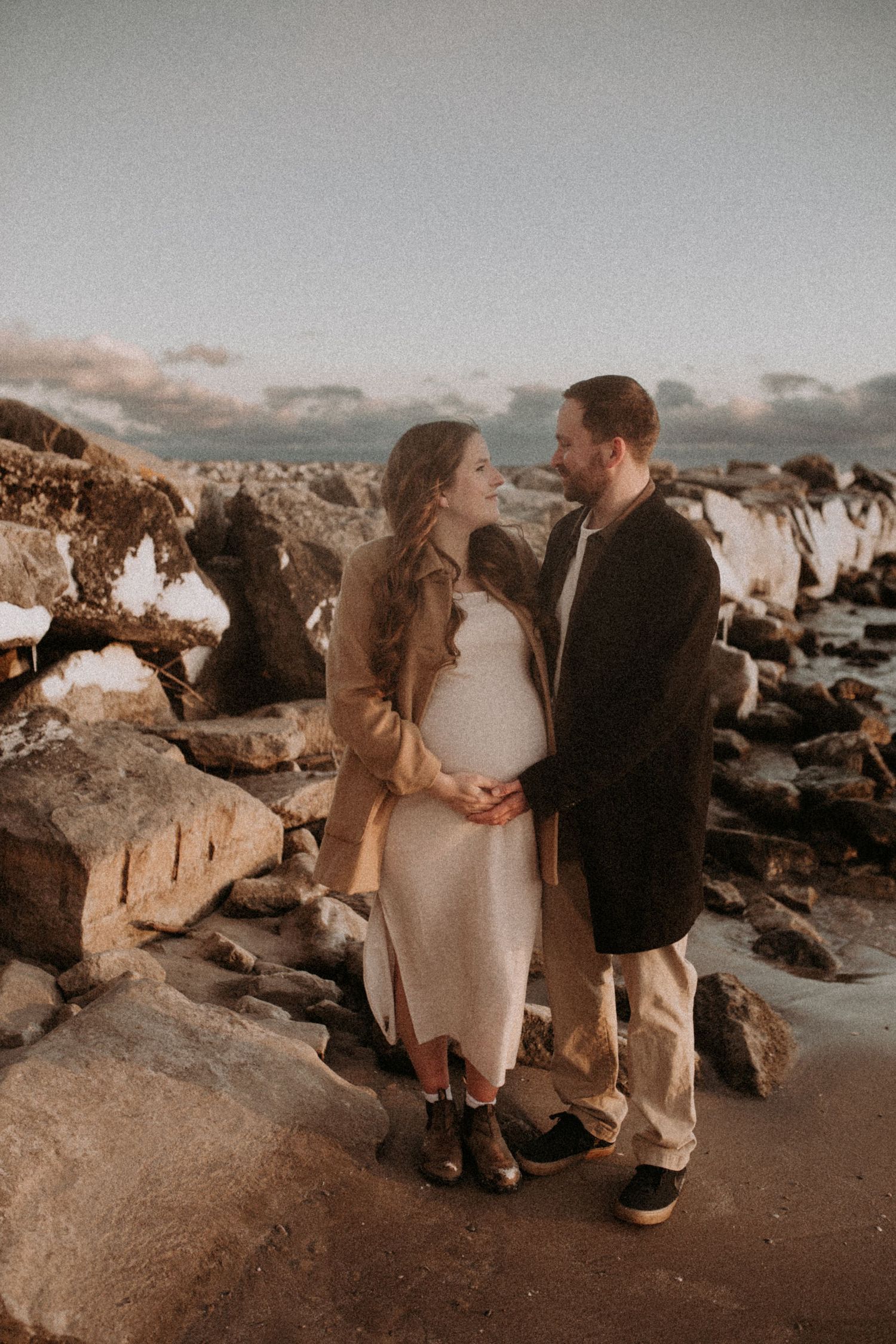 A couple shares an intimate moment near coastal rocks during a romantic sunset photoshoot on a Bowmanville Beach, Durham Region.