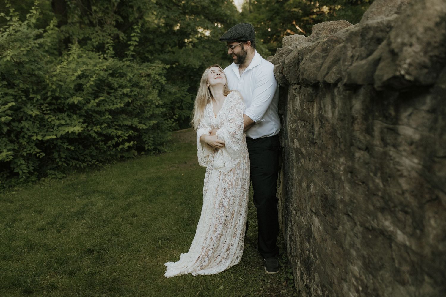 Bride in a lace gown leaning with her groom against an old stone wall by Cobourg Wedding and Elopement Photographer