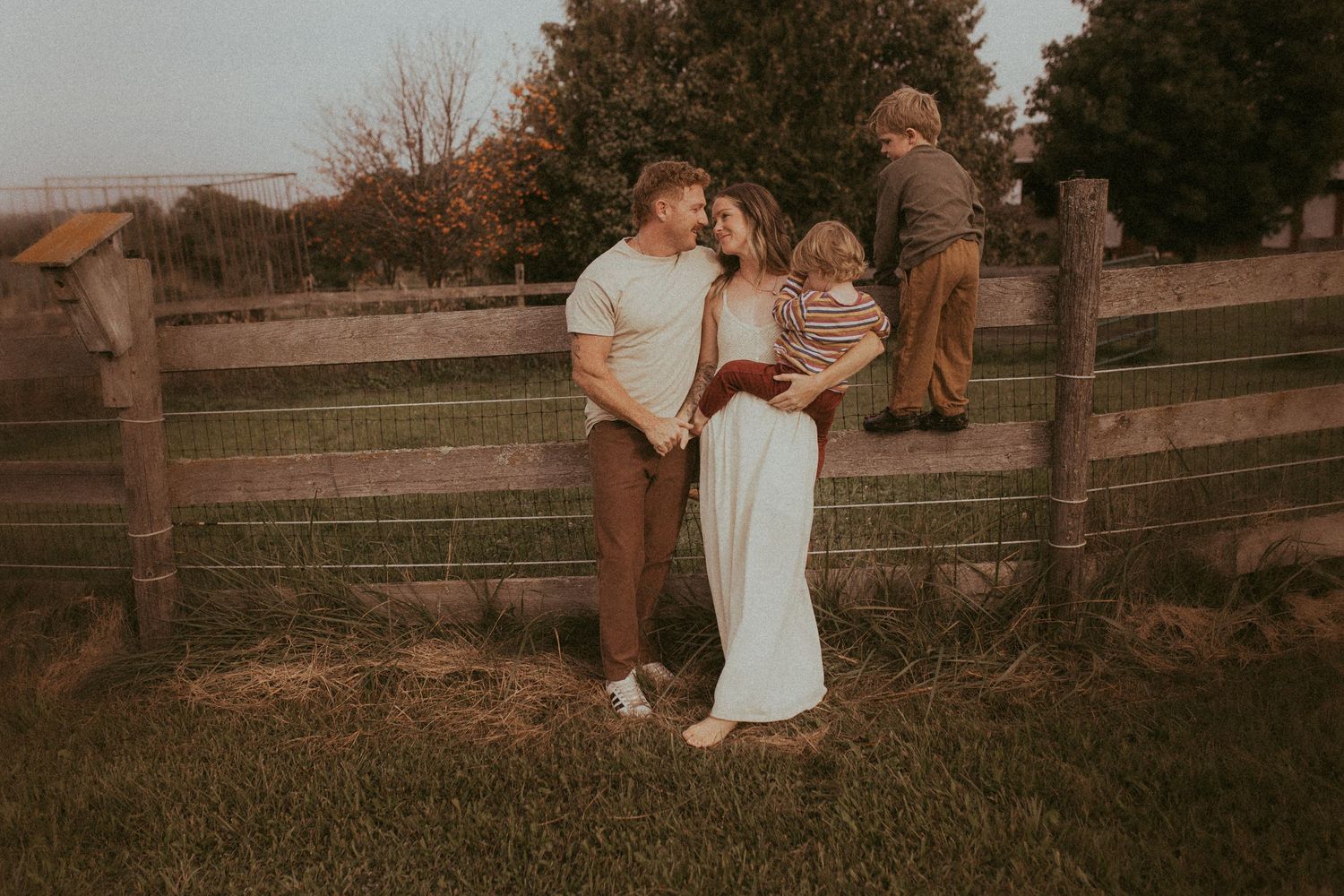 A young family leans against a rustic fence at their farm by a Durham Region family lifestyle photographer