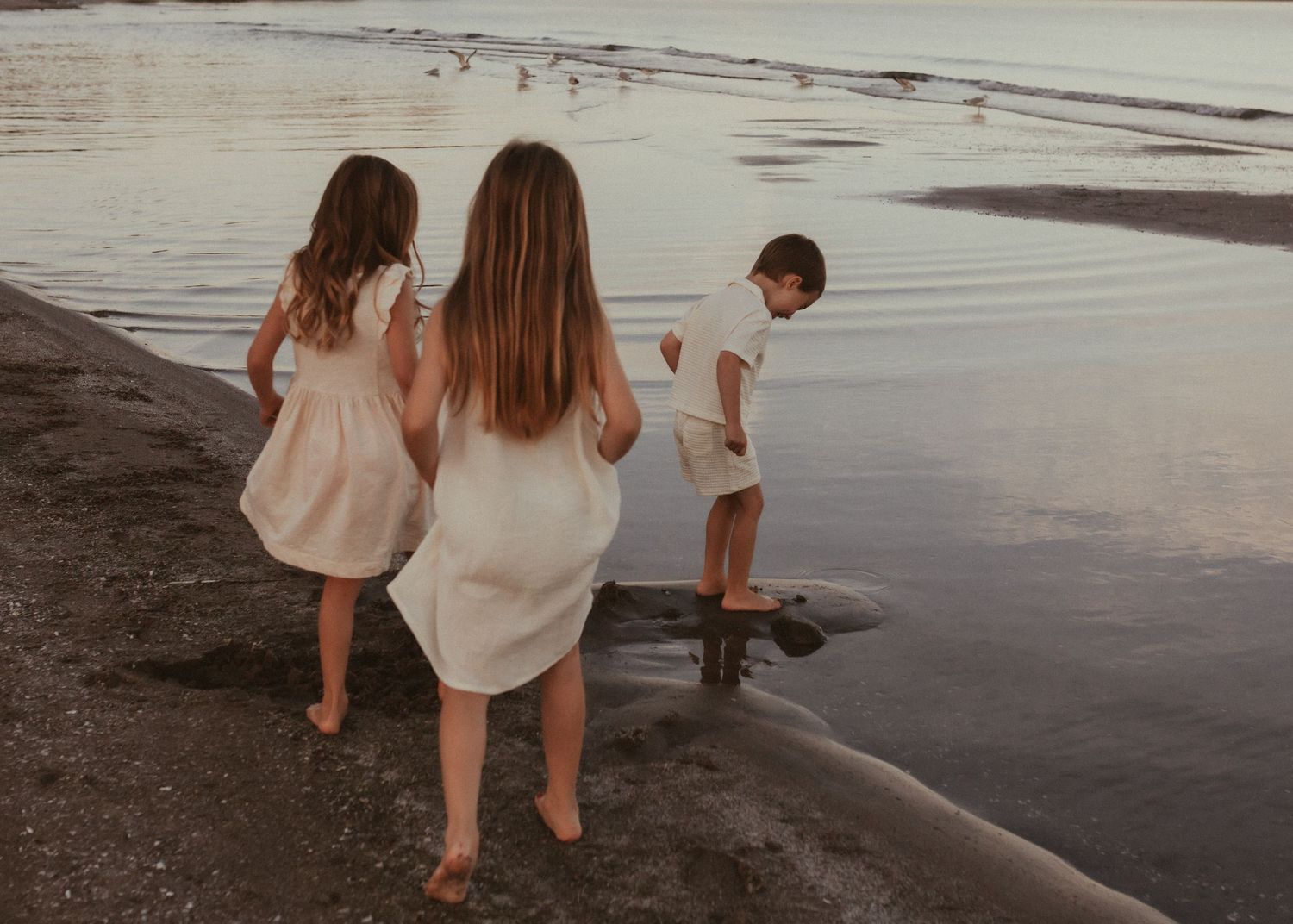 Beach session in the summer with 3 children exploring the waters along the shoreline at sunset by Bowmanville, ON family photographer.
