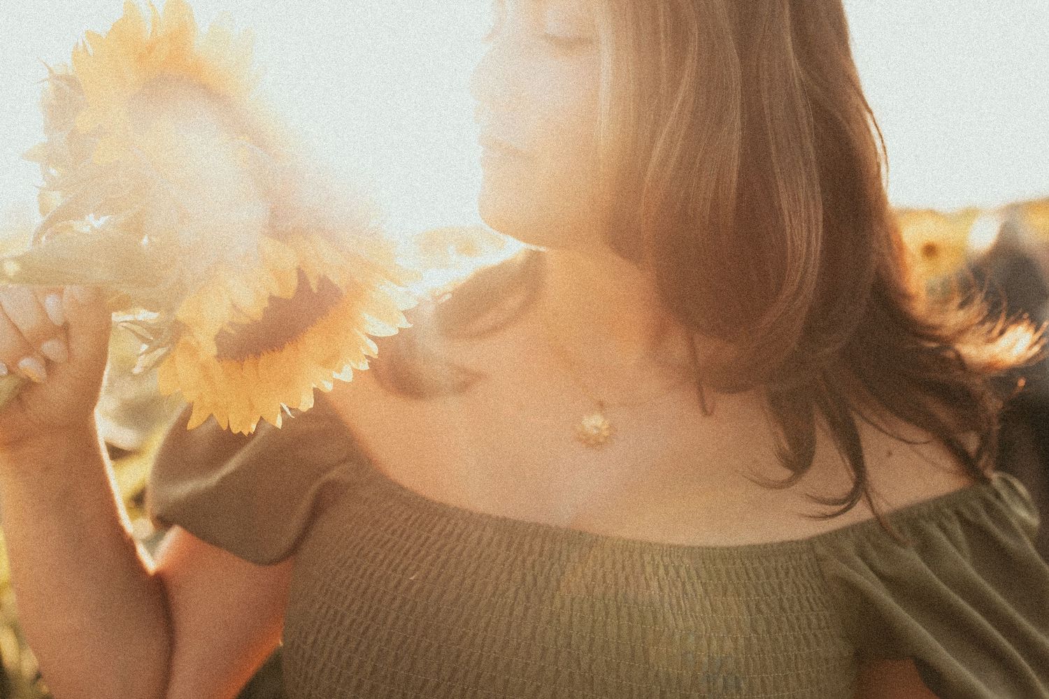 An artistic shot of a woman holding a sunflower with golden light shining through by Durham Region family photographer