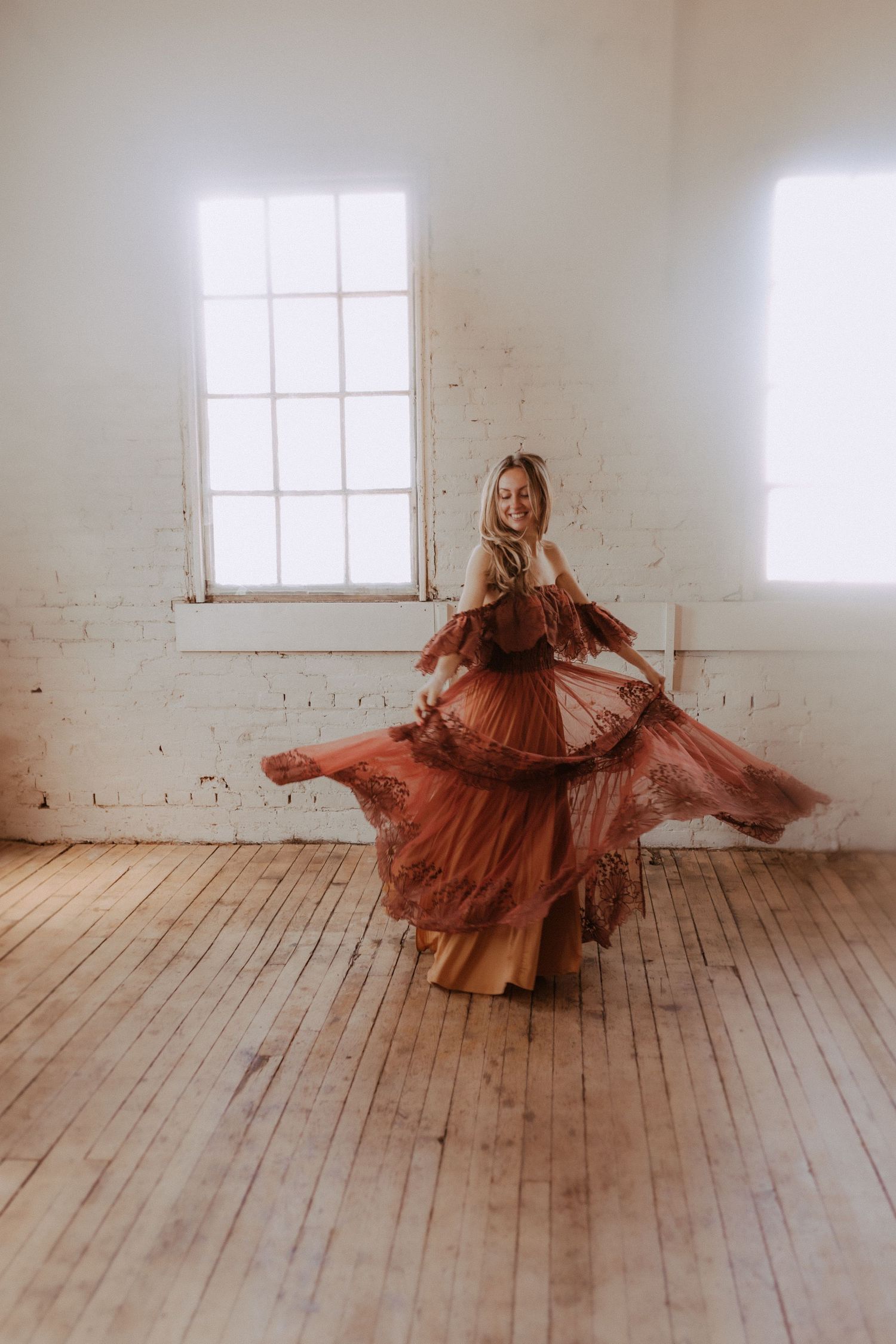 Spinning motion captured in rust-colored dress against minimalist white studio backdrop.