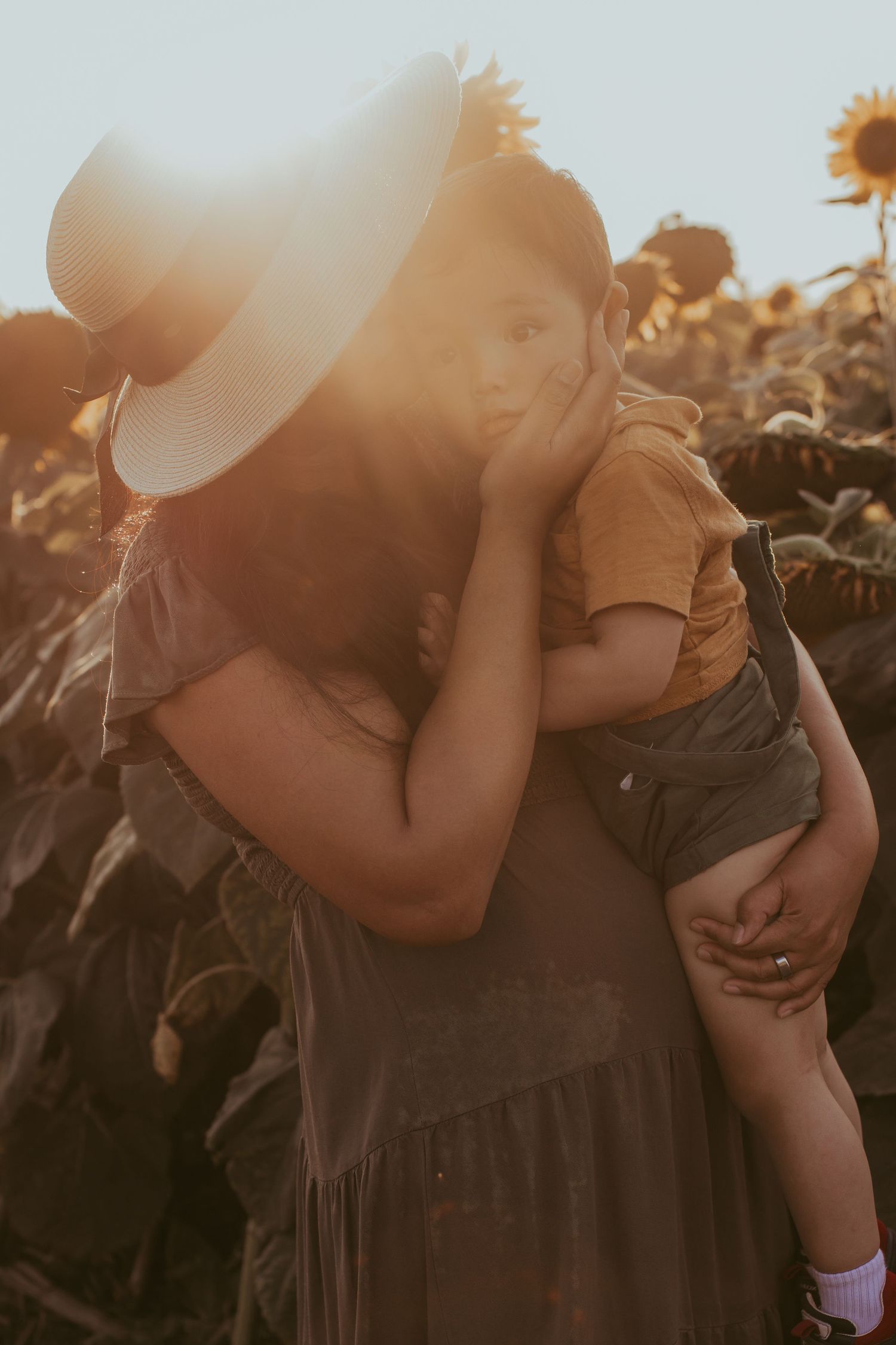 Mother gently cupping her son's face during golden hour in front of a sunflower field by Durham Region maternity photographer