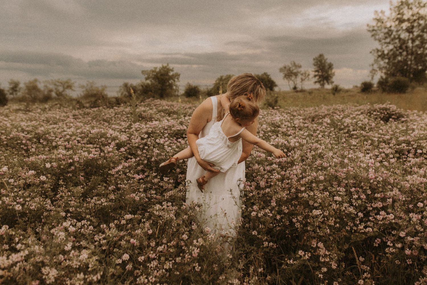 Wide-shot of a mom and daughter surrounded by wildflowers near the beach by Cobourg family photographer