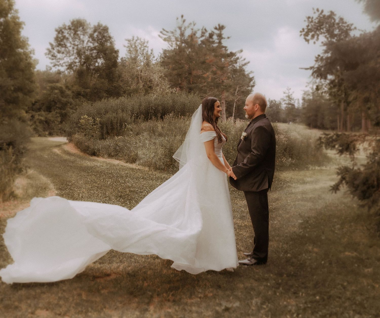 A bride and groom holding hands as her dress moves in the breeze at a park by Cobourg Wedding and Elopement Photographer