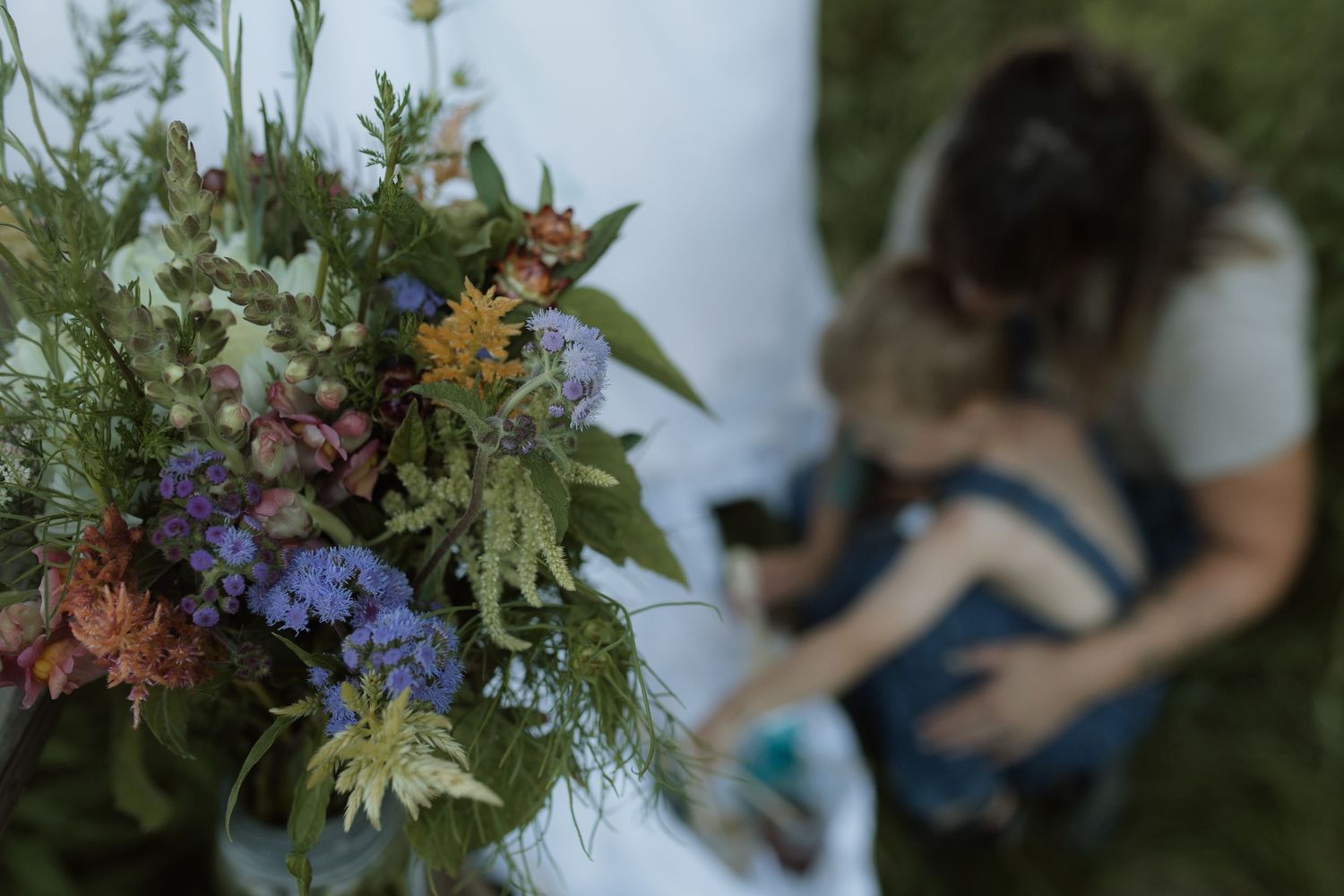 A photo of a jar of wildflowers with a blurred photo of a mom and son painting in the background by Courtice family photographer