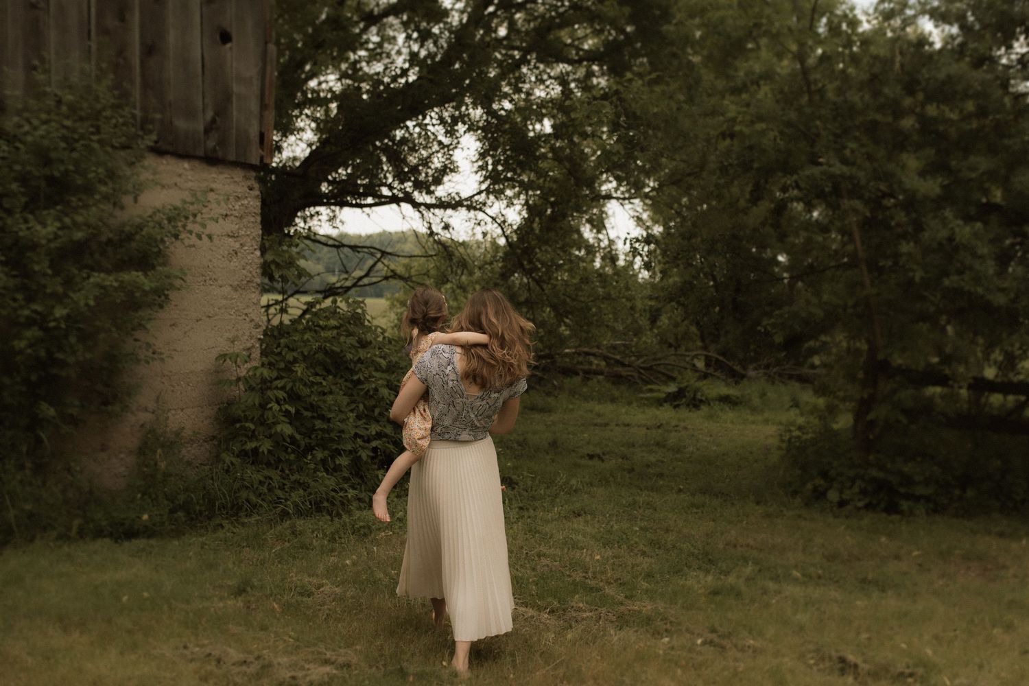 Mom walking barefoot through the grass holding her baby by Bowmanville, ON family photographer.