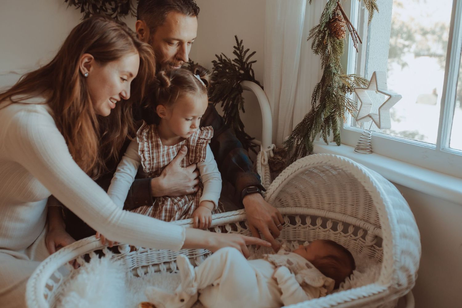 A young family surrounding the baby sleeping in a bassinet with complete love by Bowmanville, ON family photographer