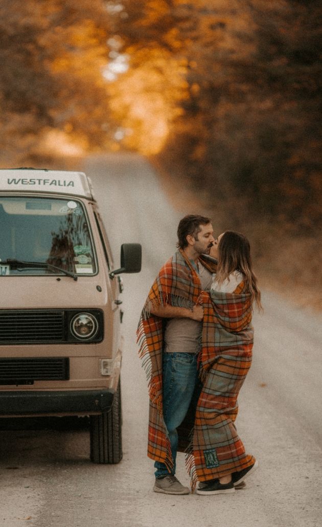 Boho couple kissing on an autumn road with a VW bus.