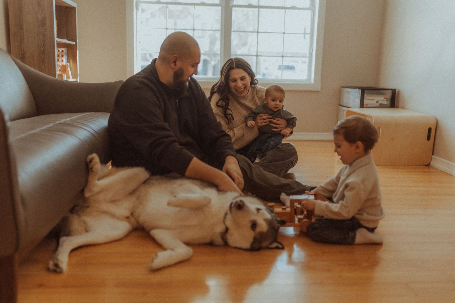 A family plays on the floor in their home while their dog basks in the joy by Durham Region maternity photographer