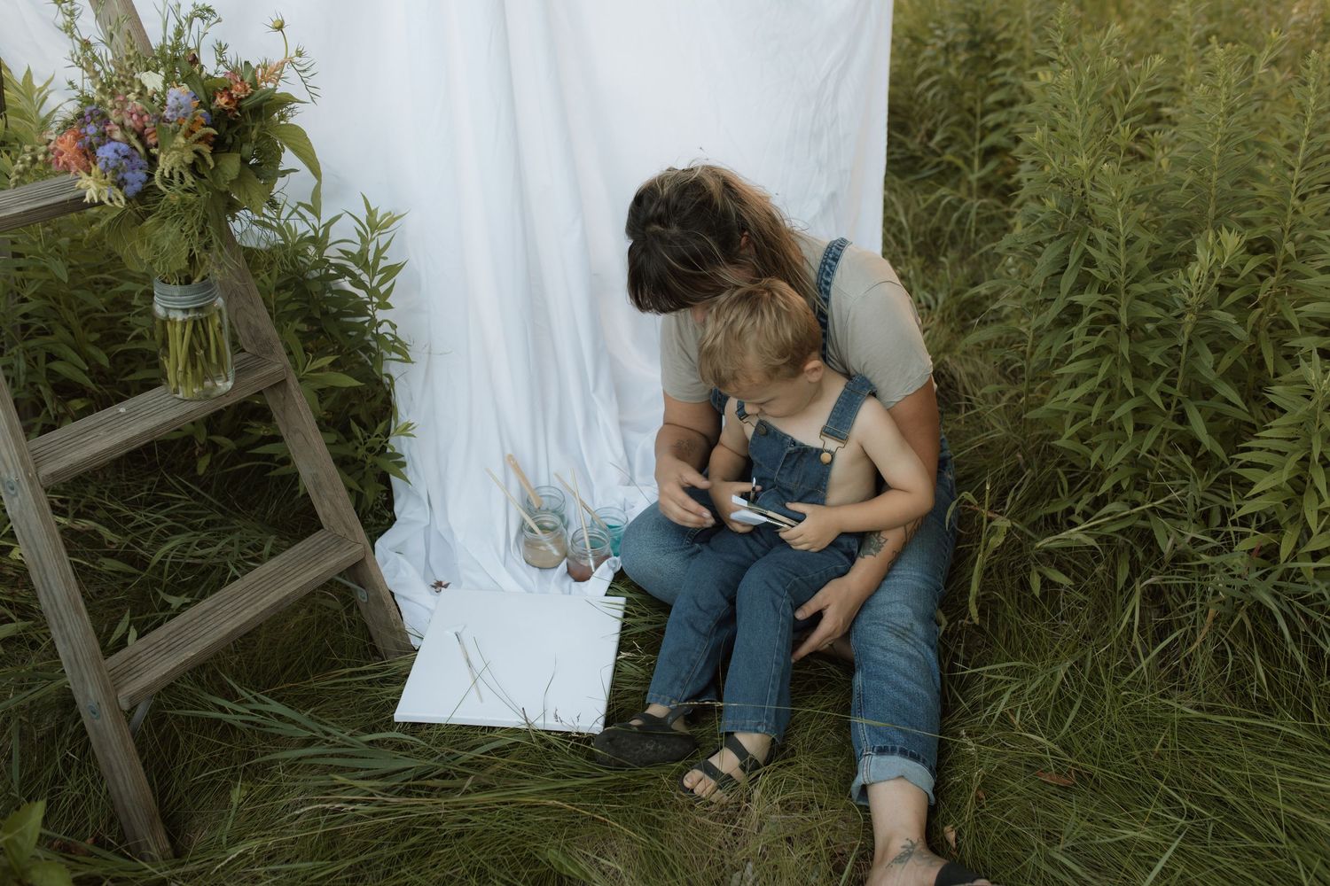 A mom holds her son in her lap and both are wearing overalls and getting ready to paint by Courtice family photographer