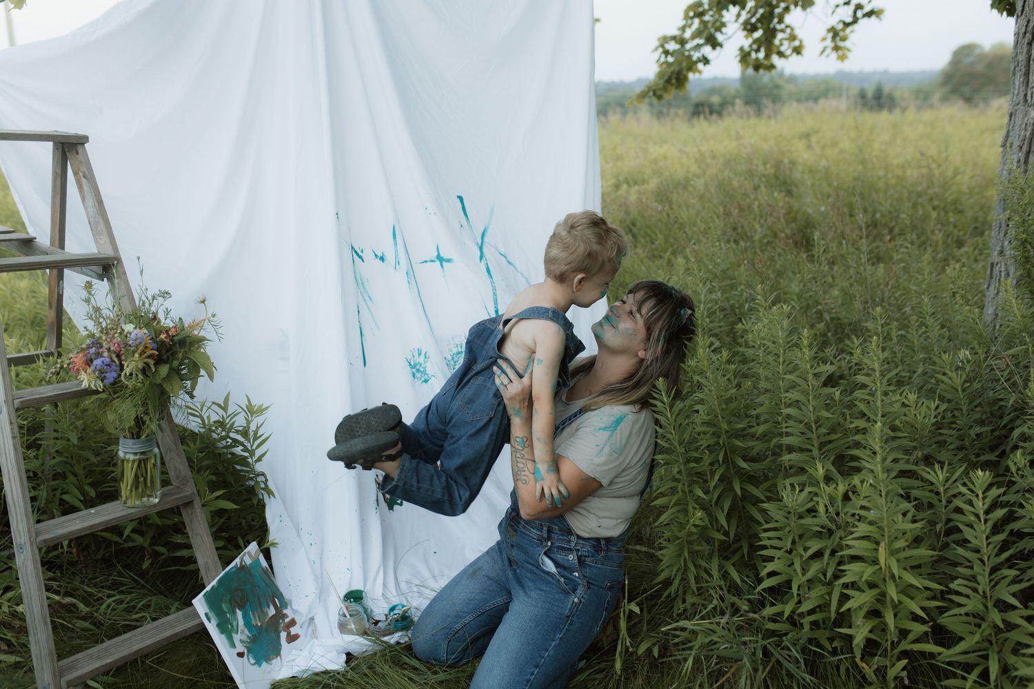 A mom joyfully lifts her son up in front of the painted sheet and canvas they were working on together by Courtice family photographer