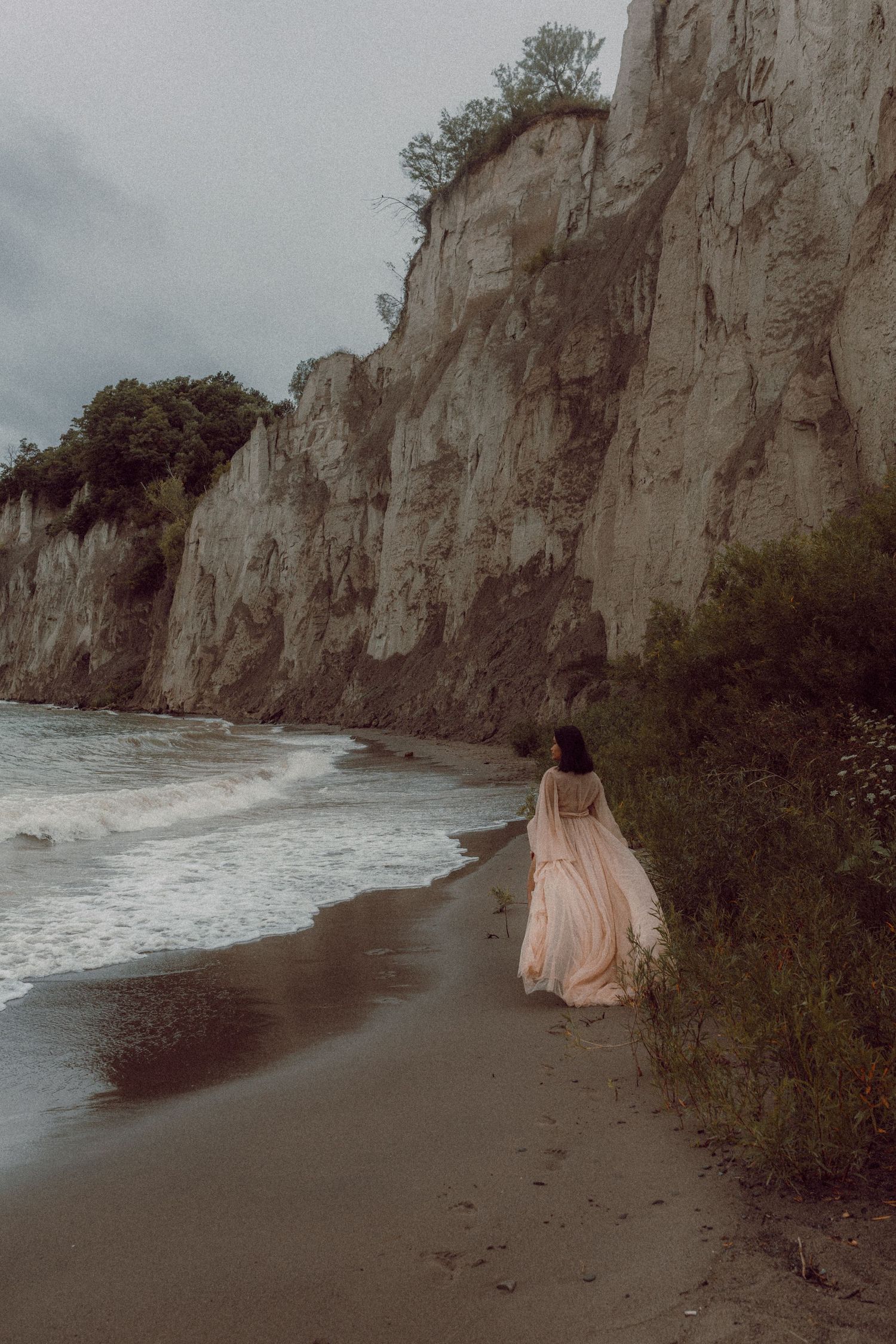Woman in a maternity dress walking along a moody beach during a Bowmanville maternity photography session.