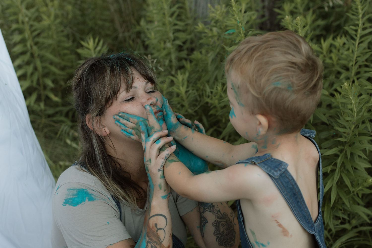 A boy puts his paint covered hands on his mom's cheeks as he laughs during a painting photo session by Courtice family photographer