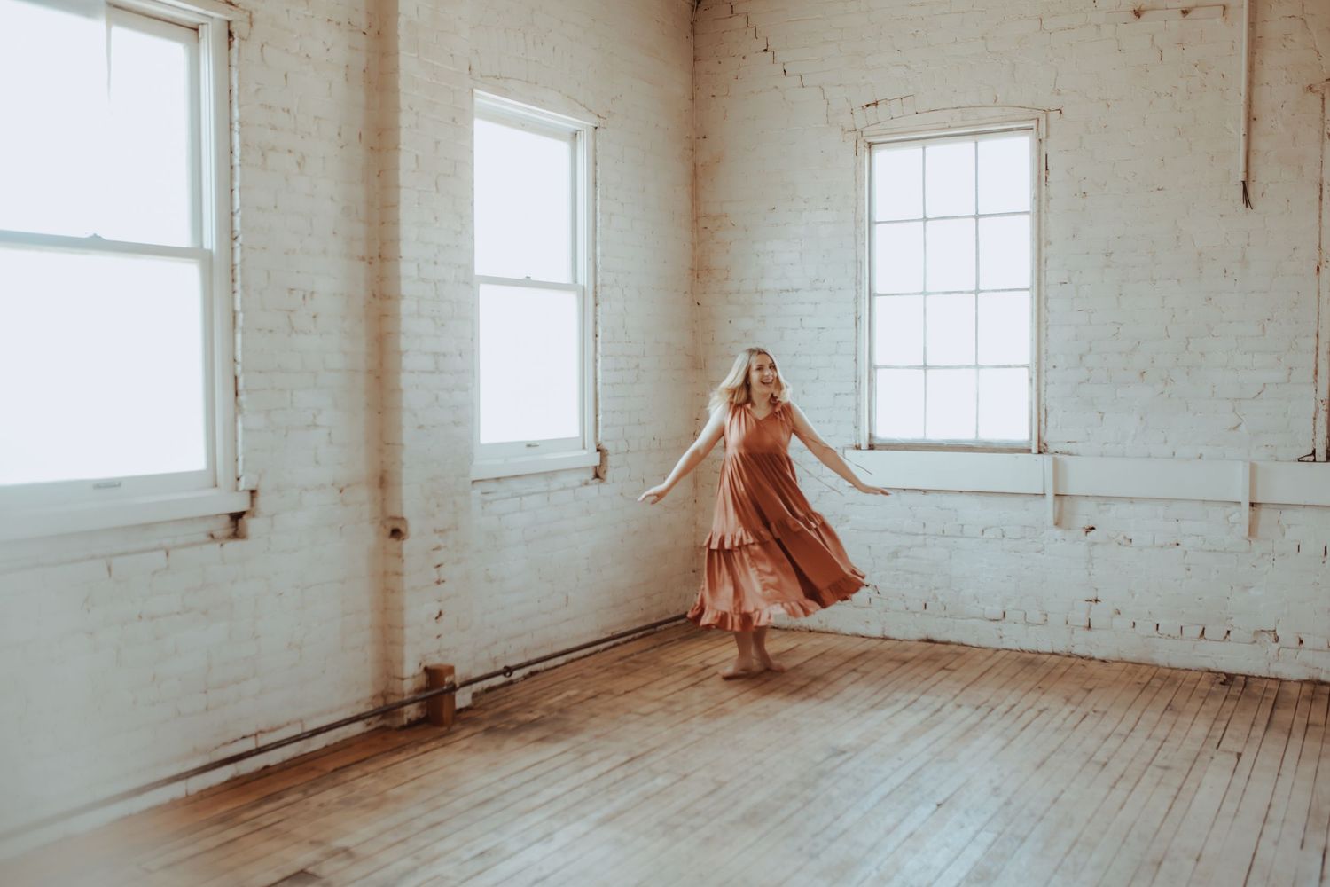 Empty white room with hardwood floors and multiple windows letting in natural light.