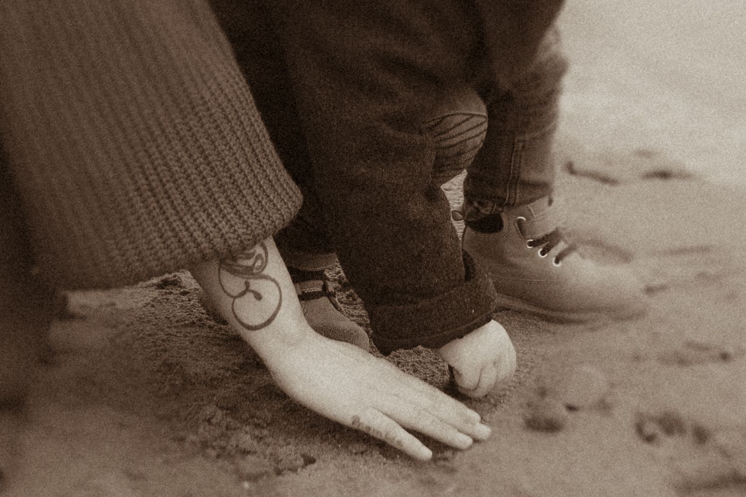 Mother and child's hands drawing in the sand during an intimate motherhood photography session in Durham Region, Ontario