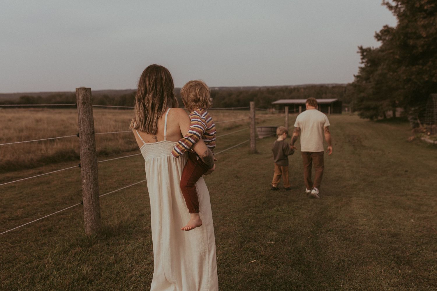 A family walks together along a fence at their farm during a Durham Region family lifestyle photography shoot.