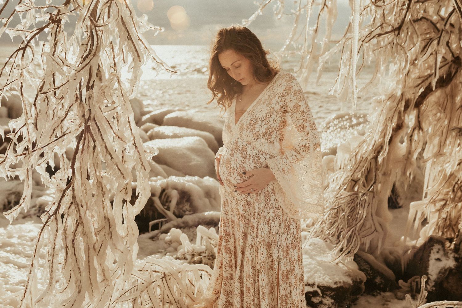 A dreamy sepia-toned photo of a person in a flowing lace dress standing among willow branches in soft natural light.
