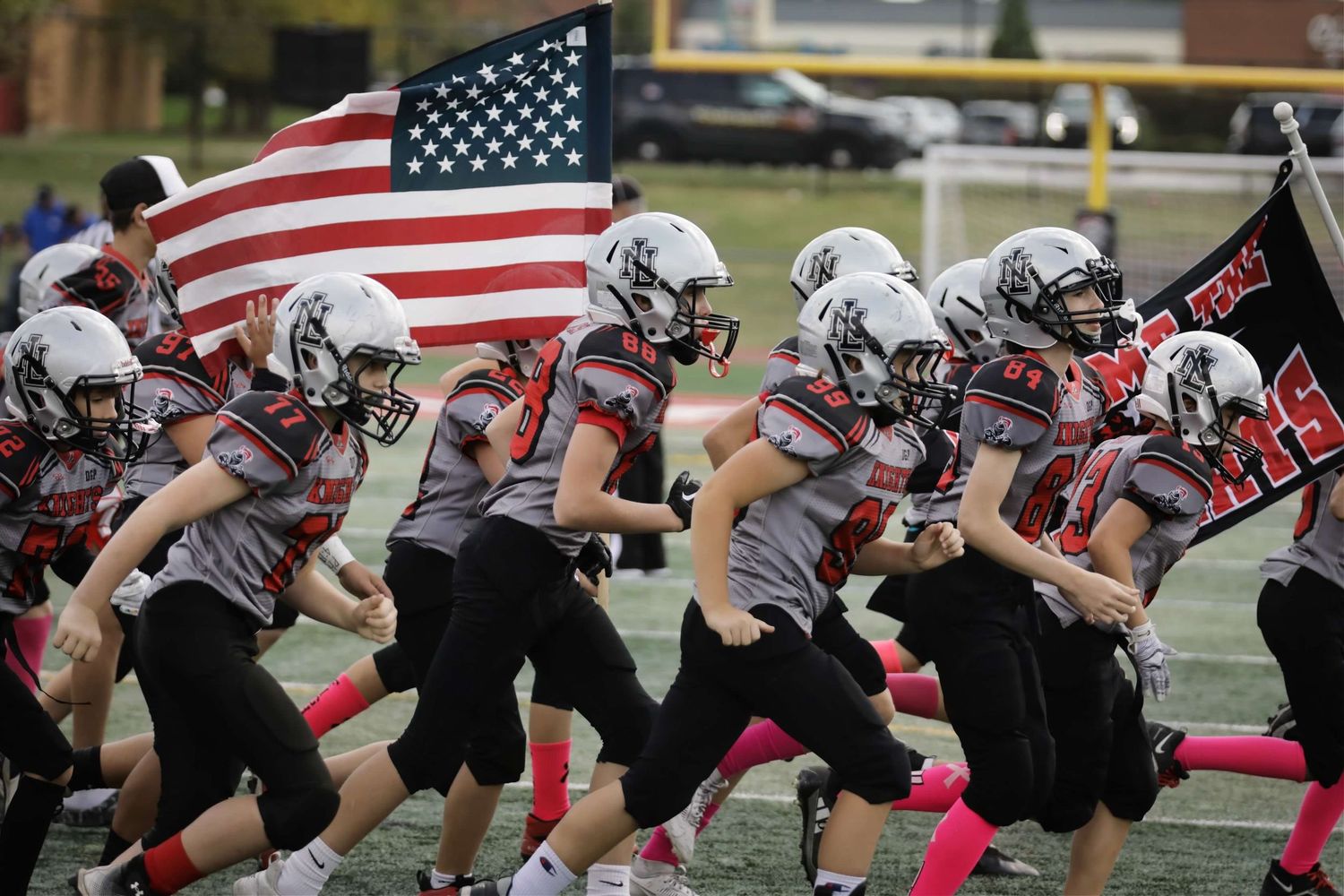 Football team lines up in formation with American flag displayed during pre-game ceremony on field.