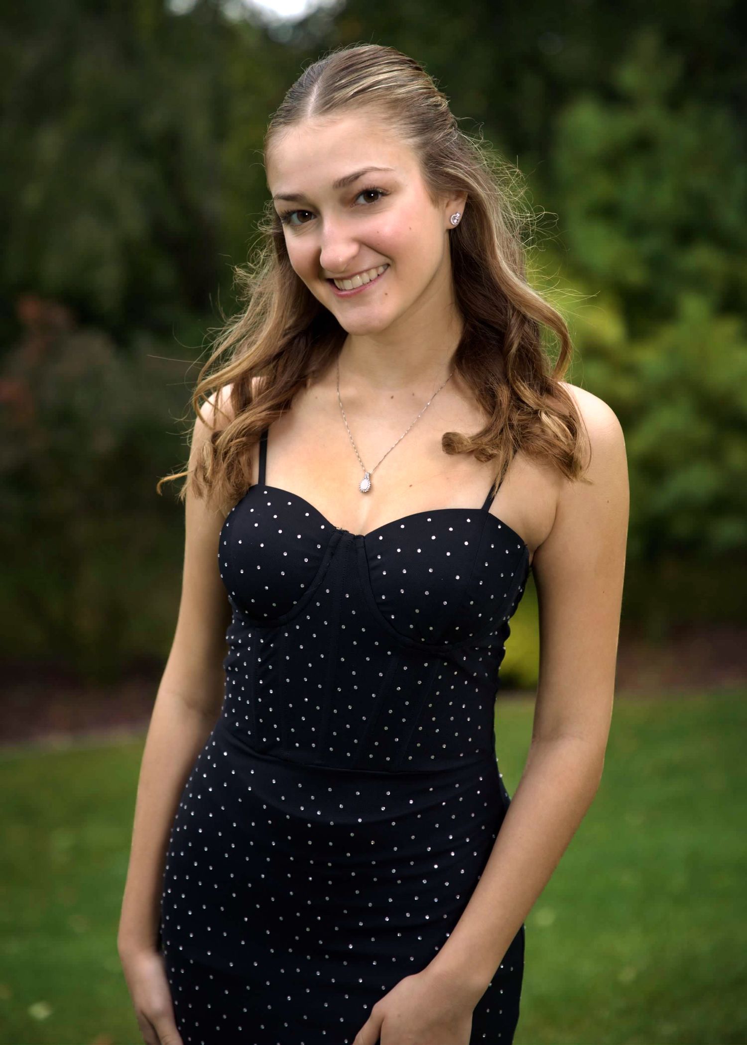 A person in a navy blue polka dot dress poses outside with natural greenery in the background.