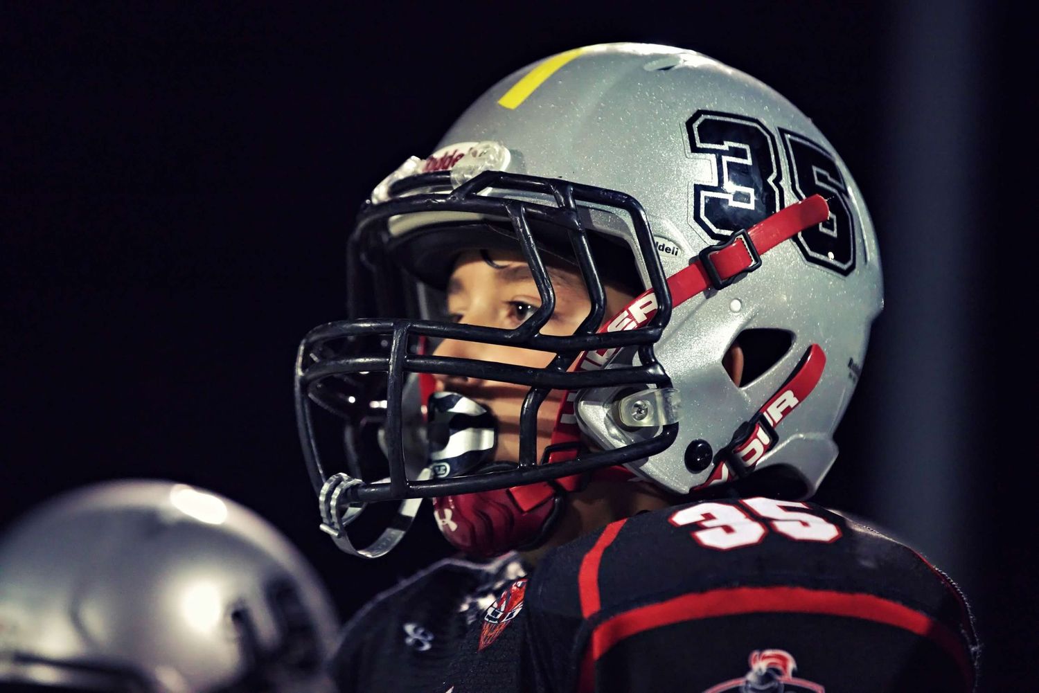 Close-up view of football players helmets showing metallic silver finish with red accents.