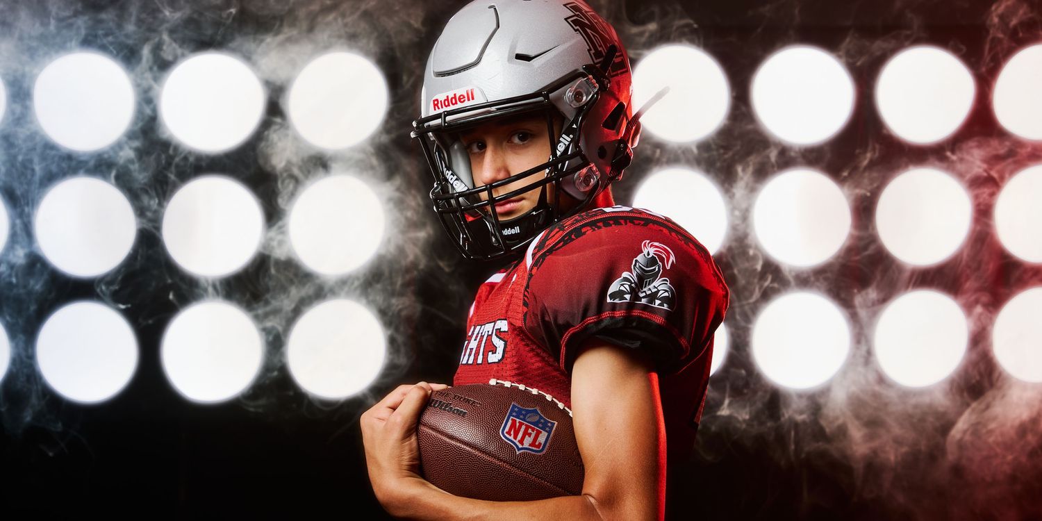 Football player strikes powerful pose in red uniform against dramatic circular stadium lighting.