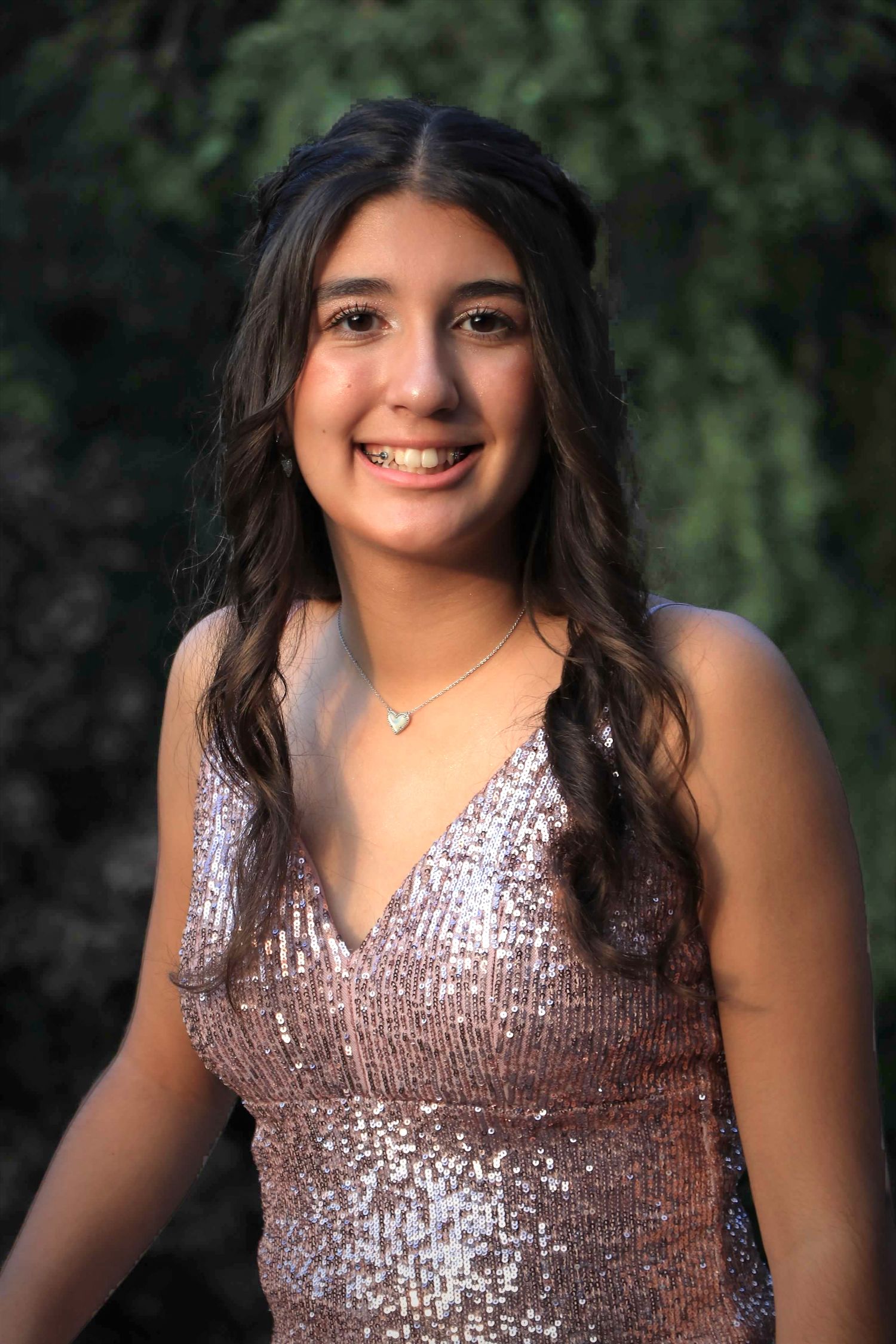 Individual in a sparkly pink sequined dress poses outdoors against a natural green background.