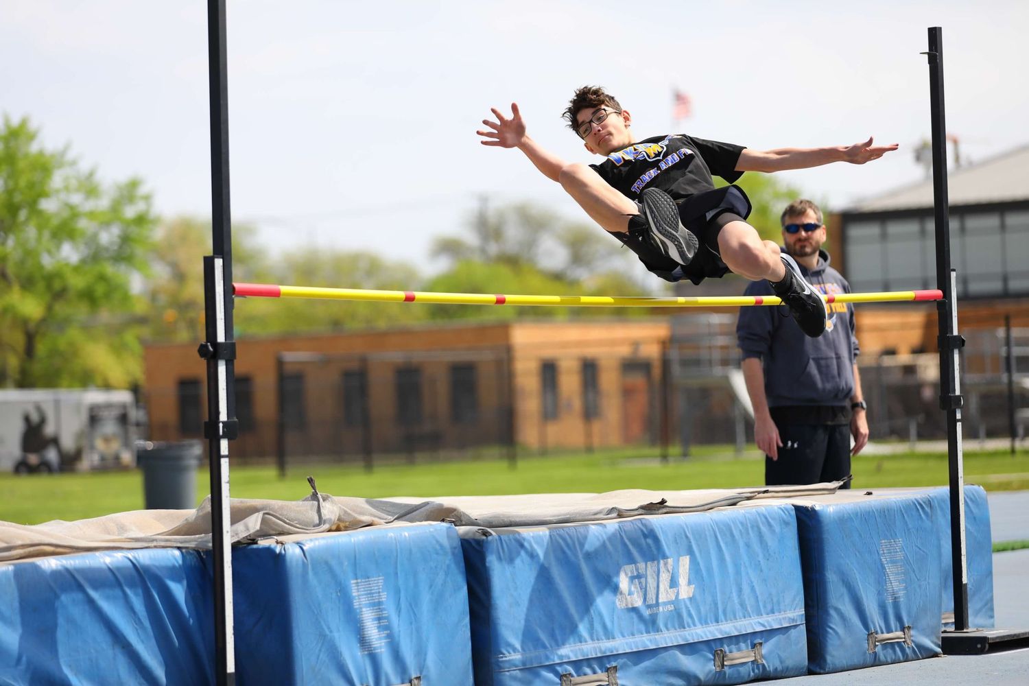 High school athlete practicing high jumps over the bar during track and field training on a sunny day.