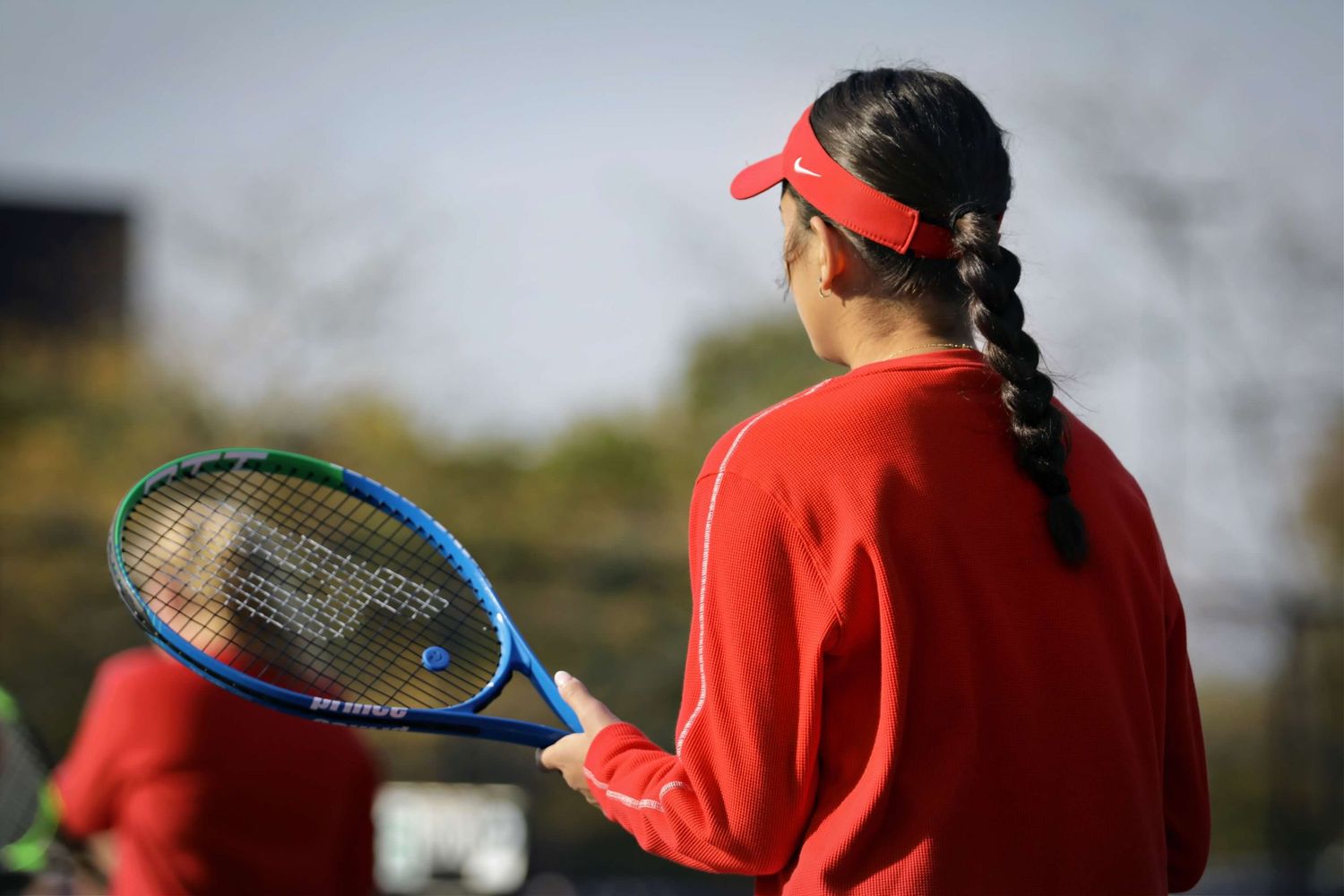 Tennis player in red attire serves the ball during an outdoor match on a sunny day.