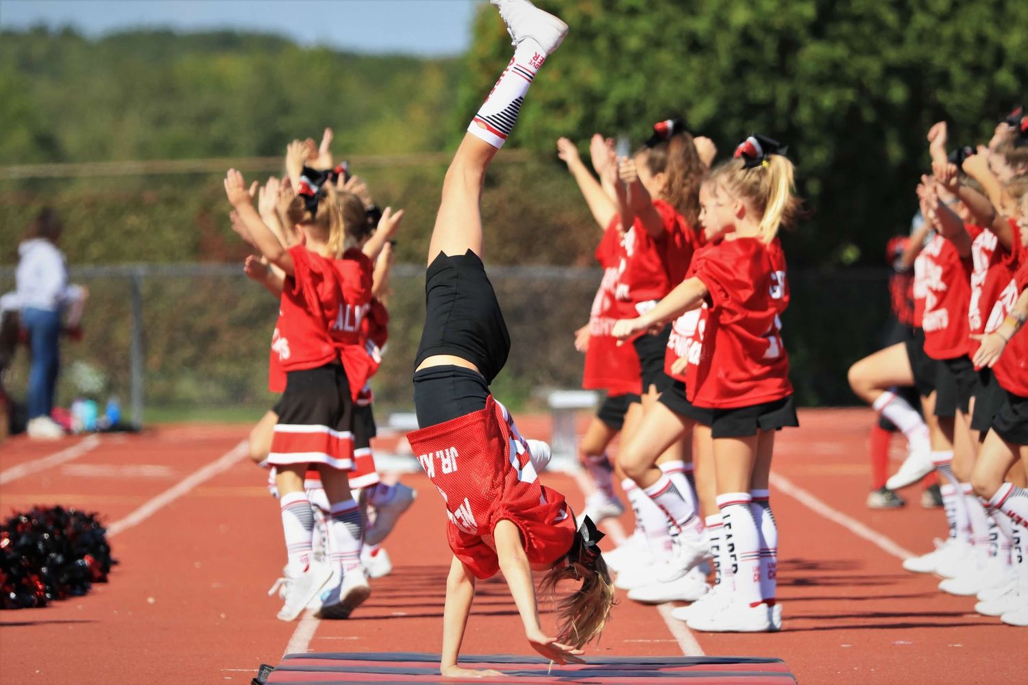 Cheerleaders execute a dynamic routine with jumps and formations on an outdoor track field.
