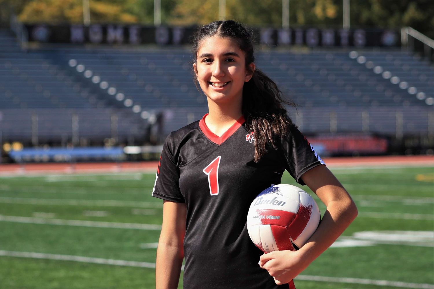 High school volleyball player in black uniform ready to serve on outdoor field during practice session.