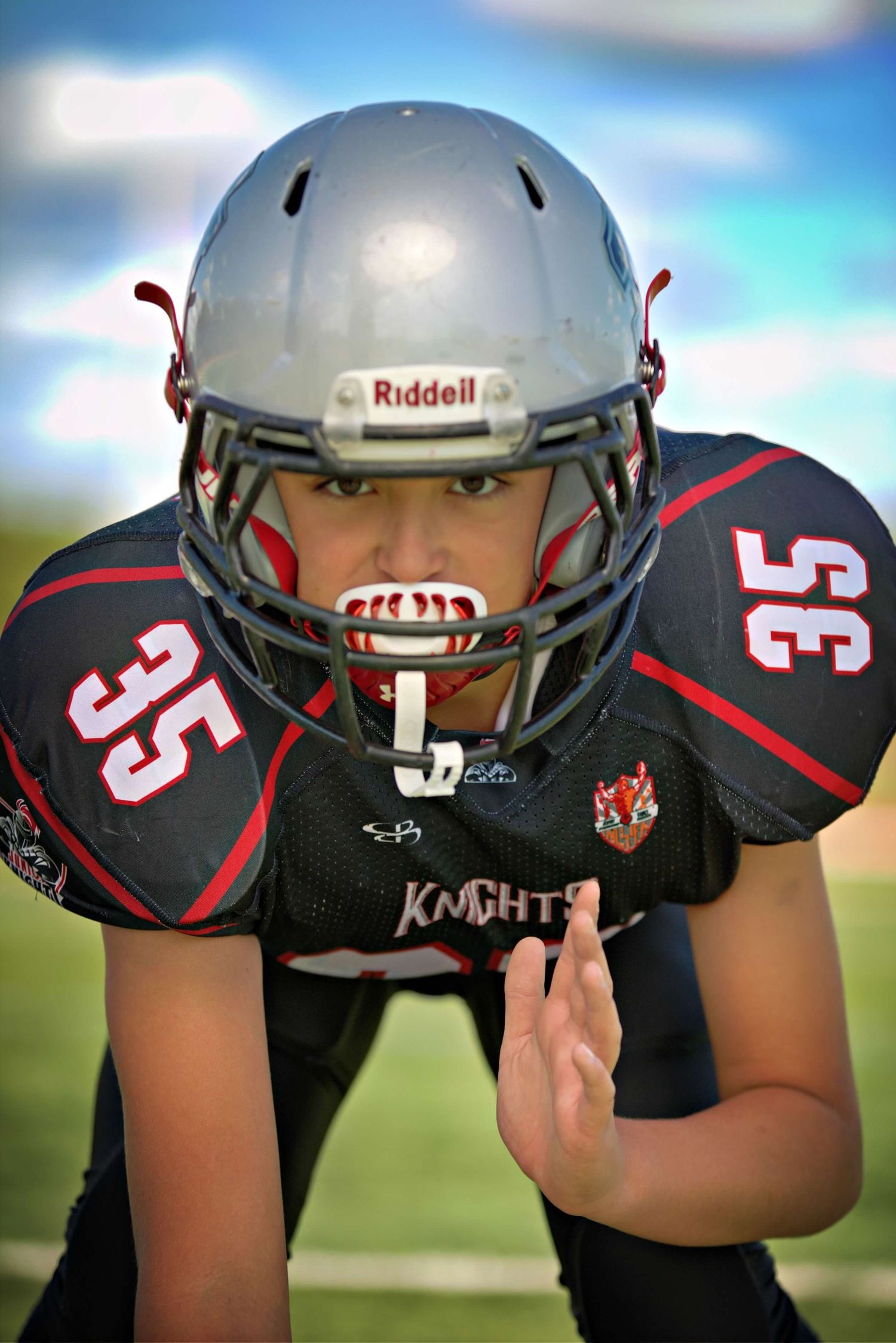 Five football players wearing black uniforms and silver helmets line up in crouched positions on the field.