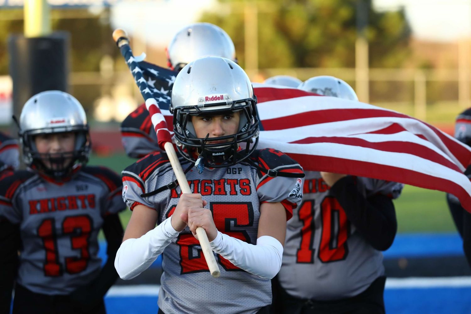 Students hold an American flag while watching a high school football game from the sidelines.