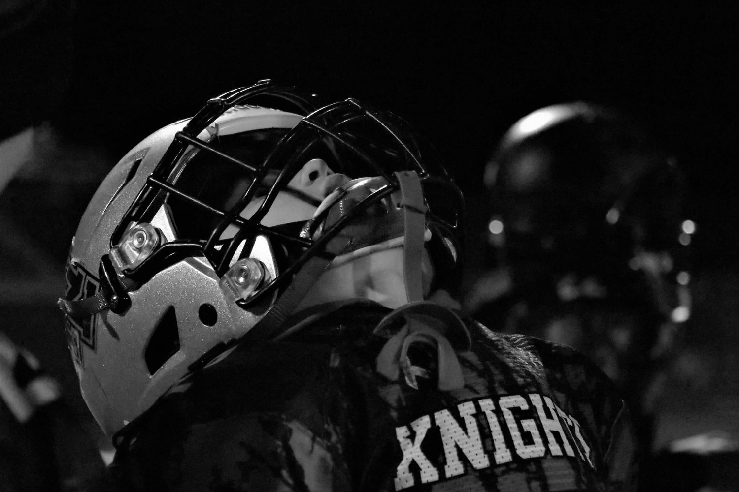 Football helmets with Knights logo shine under stadium lights during nighttime game.